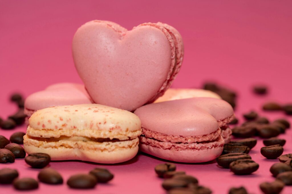 Delicious heart-shaped pink macarons and coffee beans on a vibrant pink background.