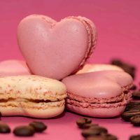 Delicious heart-shaped pink macarons and coffee beans on a vibrant pink background.